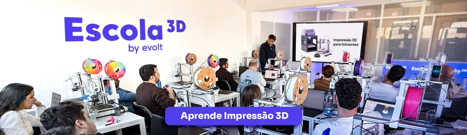 An Escola 3D class in progress, a room of people at 3D printers with the course slide on screen.